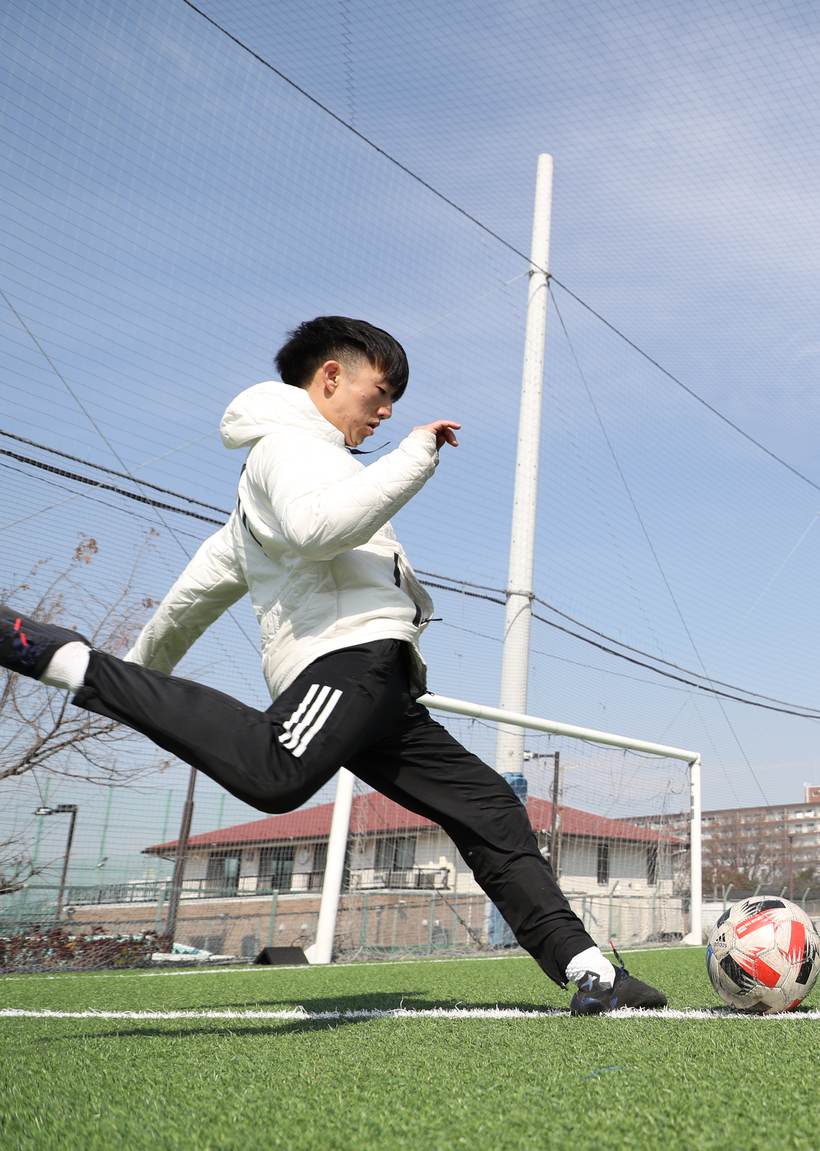 A coach striking a ball on a turf pitch, photographed from ground level